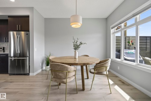 Light wood-finish flooring, large multi-pane window, built-in dark wood cabinetry, stainless steel refrigerator, and a contemporary pendant light fixture - 45 Joyal Way, St. Albert, AB - Indoor Photo Showing Dining Room