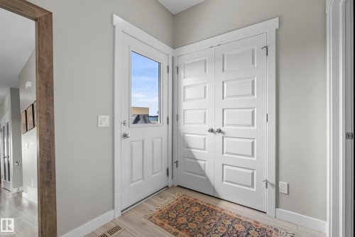 White paneled entry door with glass insert, light wood-finish flooring, and white bifold closet doors - 45 Joyal Way, St. Albert, AB - Indoor Photo Showing Other Room
