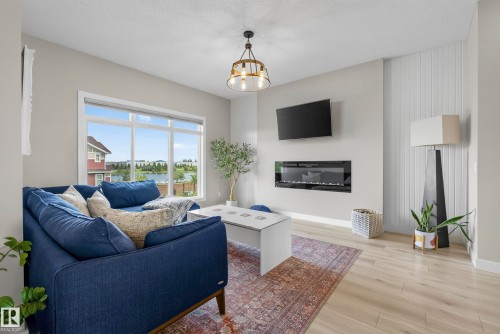 Expansive window with a water feature backdrop, light wood-finish flooring, and a contemporary wall-mounted electric fireplace - 45 Joyal Way, St. Albert, AB - Indoor Photo Showing Living Room With Fireplace