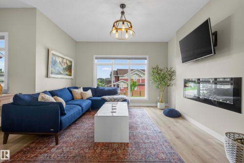 Spacious living area featuring light wood-finish flooring, a contemporary electric fireplace, a prominent window, and a modern ceiling fixture - 45 Joyal Way, St. Albert, AB - Indoor Photo Showing Living Room