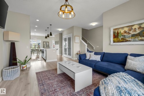 Open-concept living area featuring a navy upholstered sectional sofa, white ottoman coffee table, and wood-finish flooring throughout - 45 Joyal Way, St. Albert, AB - Indoor Photo Showing Living Room