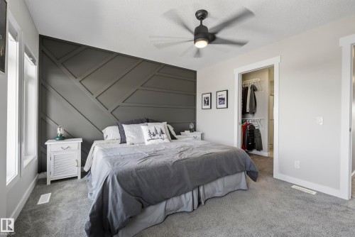 Accent wall with geometric paneling, ceiling fan with integrated lighting, carpeted flooring, and built-in closet with shelving - 45 Joyal Way, St. Albert, AB - Indoor Photo Showing Bedroom