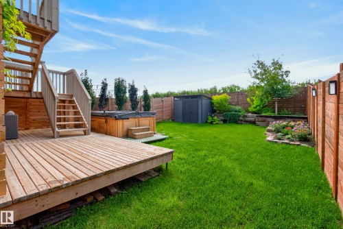 Expansive wooden deck with staircase, hot tub, lush lawn, raised garden beds, and secure privacy fencing with accent lighting - 45 Joyal Way, St. Albert, AB - Outdoor With Deck Patio Veranda