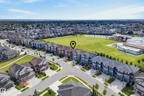 Neighborhood setting featuring a large open green space, rows of multi-story townhomes, and single-family residences with attached garages - 45 Joyal Way, St. Albert, AB - Outdoor With View