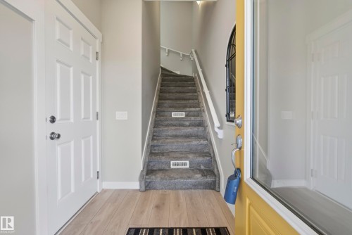 Light wood-finish flooring, crisp white trim, paneled interior door, carpeted staircase, and decorative arched window with ironwork - 45 Joyal Way, St. Albert, AB - Indoor Photo Showing Other Room