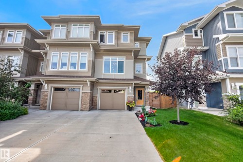 Contemporary townhouse exterior featuring multiple windows, a dual garage, stone accents, and a well-maintained lawn - 45 Joyal Way, St. Albert, AB - Outdoor With Facade