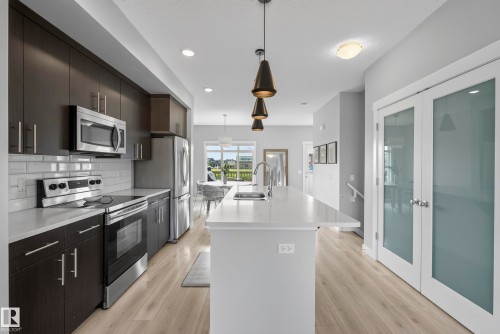 Modern kitchen featuring stainless steel appliances, dark wood-finish cabinetry, light countertops, and a subway tile backsplash - 45 Joyal Way, St. Albert, AB - Indoor Photo Showing Kitchen With Upgraded Kitchen