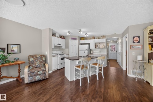 Kitchen and living area featuring wood-finish flooring, light gray wall paint, white cabinetry, a kitchen island with seating, and white appliances - #7 155 Crocus Cr, Sherwood Park, AB - Indoor