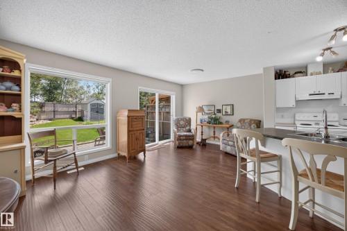 Open-concept living space featuring wood-finish flooring, a kitchen island with seating, white cabinetry, and a sliding glass door to the exterior - #7 155 Crocus Cr, Sherwood Park, AB - Indoor