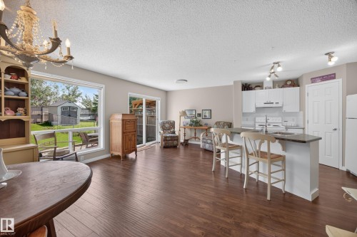Open-concept living space featuring wood-finish flooring throughout, a white kitchen with a dark countertop and breakfast bar, and a sliding glass door providing backyard access - #7 155 Crocus Cr, Sherwood Park, AB - Indoor