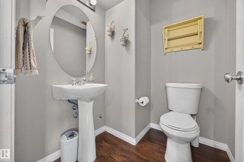 Powder room featuring a white pedestal sink, an oval mirror, and wood-finish flooring - #7 155 Crocus Cr, Sherwood Park, AB - Indoor Photo Showing Bathroom