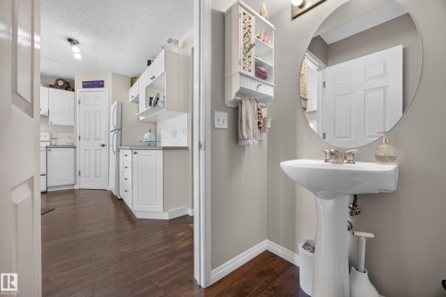 Pedestal sink with brushed nickel faucet, round mirror, and wood-finish flooring - #7 155 Crocus Cr, Sherwood Park, AB - Indoor Photo Showing Bathroom
