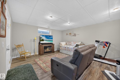 Finished lower level featuring wood-finish flooring, light grey painted walls, a drop ceiling with recessed lighting, and a window with horizontal blinds - #7 155 Crocus Cr, Sherwood Park, AB - Indoor With Fireplace