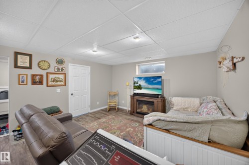 Spacious room featuring wood-finish flooring, light gray walls, a drop ceiling with recessed lighting, and a window with horizontal blinds - #7 155 Crocus Cr, Sherwood Park, AB - Indoor With Fireplace