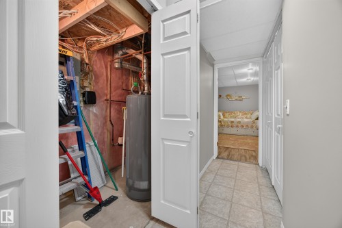 Basement utility area featuring exposed wood joists and a water heater, with a separate finished area showing wood-finish flooring - #7 155 Crocus Cr, Sherwood Park, AB - Indoor Photo Showing Other Room