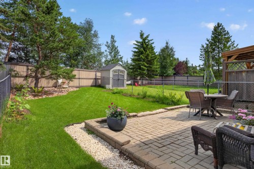 Spacious backyard featuring a paver patio with raised paver edging, an expansive lawn, mature perimeter trees, and a storage shed - #7 155 Crocus Cr, Sherwood Park, AB - Outdoor With Backyard