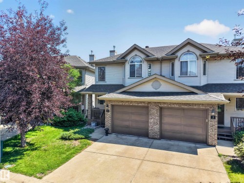 Exterior featuring light-toned siding and a prominent two-car garage with brick-accented pillars - #7 155 Crocus Cr, Sherwood Park, AB - Outdoor With Facade