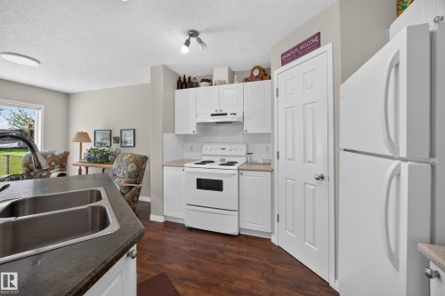 Kitchen featuring white cabinetry, a double basin stainless steel sink, a smooth-top electric range, a white refrigerator, and wood-finish flooring - #7 155 Crocus Cr, Sherwood Park, AB - Indoor Photo Showing Kitchen With Double Sink