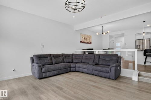 Spacious living area featuring light wood-finish flooring, recessed lighting, and a contemporary black chandelier - 23027 96 Avenue Nw, Edmonton, AB - Indoor Photo Showing Living Room