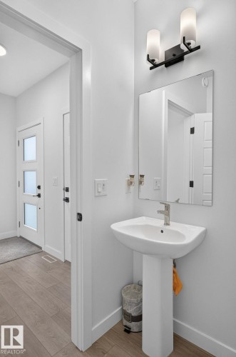 Pedestal sink with a single-handle faucet, rectangular mirror, and a two-light vanity fixture - 23027 96 Avenue Nw, Edmonton, AB - Indoor Photo Showing Bathroom