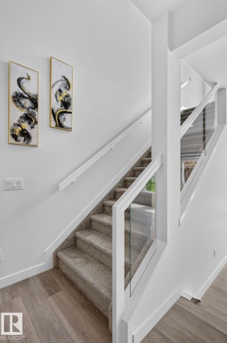 Staircase featuring light gray carpeted treads and risers, white painted stringers, and a contemporary glass railing system with white posts - 23027 96 Avenue Nw, Edmonton, AB - Indoor Photo Showing Other Room
