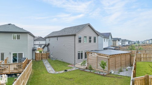 Rear exterior with light gray siding, featuring a wood-slat enclosed structure, a stone pathway, a manicured lawn, and privacy fencing - 23027 96 Avenue Nw, Edmonton, AB - Outdoor With Deck Patio Veranda