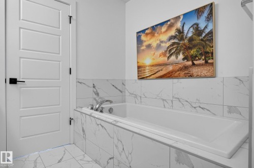 Built-in soaking tub featuring chrome fixtures, surrounded by large format white tiles with grey veining, and a coordinating tiled floor - 23027 96 Avenue Nw, Edmonton, AB - Indoor Photo Showing Bathroom