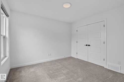 Interior room featuring a double window, light-colored walls, gray carpet, and a pair of paneled doors with black hardware - 23027 96 Avenue Nw, Edmonton, AB - Indoor Photo Showing Other Room