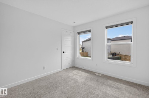 Room featuring two large windows, light gray carpeting, crisp white walls, and a contemporary five-panel interior door with matte black hardware - 23027 96 Avenue Nw, Edmonton, AB - Indoor Photo Showing Other Room