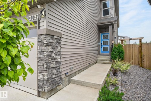 Modern exterior featuring horizontal siding in a neutral tone, complemented by a vibrant blue entry door with three frosted glass panels - 23027 96 Avenue Nw, Edmonton, AB - Outdoor