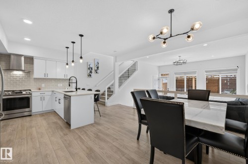 Open-concept living space featuring wood-finish flooring, a contemporary kitchen with white cabinetry and stainless steel appliances, a kitchen island with pendant lighting, a dining area with a marble-top table, and a modern chandelier - 23027 96 Avenue Nw, Edmonton, AB - Indoor
