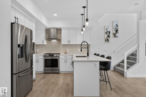 Modern kitchen featuring stainless steel appliances, white cabinetry, a tiled backsplash, and wood-finish flooring - 23027 96 Avenue Nw, Edmonton, AB - Indoor Photo Showing Kitchen With Stainless Steel Kitchen With Upgraded Kitchen