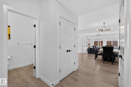Open-concept interior featuring wood-finish flooring, white panel doors with black hardware, and a modern linear chandelier - 23027 96 Avenue Nw, Edmonton, AB - Indoor Photo Showing Other Room