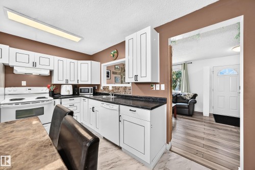 White cabinetry, dark stone-finish countertops, tile backsplash, tile flooring, and a white paneled door with an arched window - 64 Habitat Crescent Nw, Edmonton, AB - Indoor Photo Showing Kitchen
