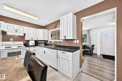 White cabinetry, dark stone-finish countertops, tile backsplash, tile flooring, and a white paneled door with an arched window - 