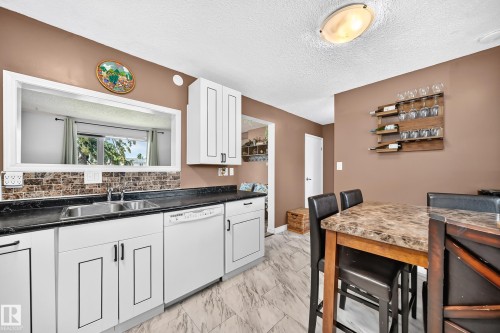 White cabinetry, black countertops, stainless steel double basin sink, tile backsplash, and light-toned flooring - 64 Habitat Crescent Nw, Edmonton, AB - Indoor Photo Showing Kitchen With Double Sink