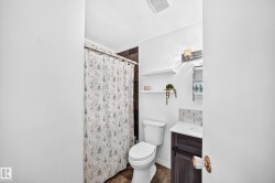 Bathroom featuring a built-in vanity with a white countertop, patterned tile backsplash, wall-mounted light fixture, and wood-finish flooring - 
