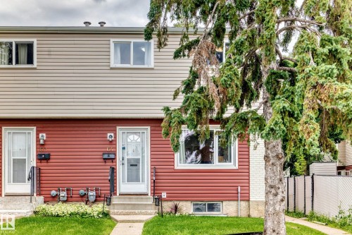 Two-story duplex featuring horizontal siding, individual entryways, and a front yard with mature landscaping - 64 Habitat Crescent Nw, Edmonton, AB - Outdoor