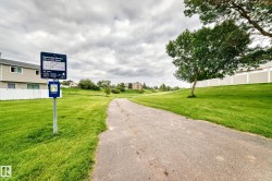 Paved pathway bordered by manicured green spaces and mature trees - 