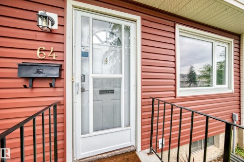 Red horizontal siding exterior with a white storm door, white window trim, and a black metal railing - 64 Habitat Crescent Nw, Edmonton, AB - Outdoor With Exterior