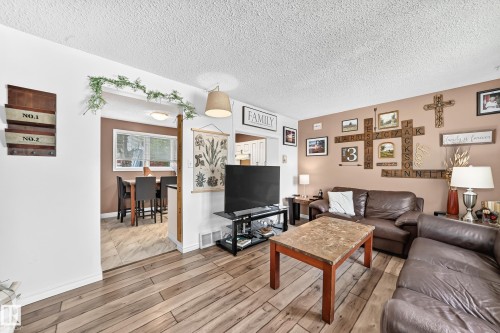 Wood-finish flooring throughout, with a dining area featuring a window, and a living area with warm-toned walls - 64 Habitat Crescent Nw, Edmonton, AB - Indoor Photo Showing Living Room