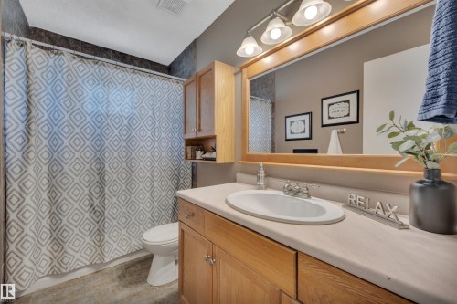 Bathroom featuring a single vanity, wood-finish cabinetry, built-in mirror with integrated lighting, and a shower/tub combination with tile surround - 148 Corinthia Drive, Leduc, AB - Indoor Photo Showing Bathroom