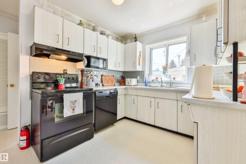Kitchen featuring white cabinetry, a black range, overhead microwave, a west-facing window above the sink, and light-colored flooring - 3824 111B Street Nw, Edmonton, AB - Indoor Photo Showing Kitchen