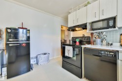Kitchen featuring white upper cabinetry, light blue square tile backsplash, white countertops, a black range, and a black dishwasher and fridge. - 