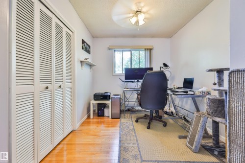 Third bedroom on main level, but can be used as an office featuring wood-finish flooring, louvered bi-fold closet doors, a single window facing east with blinds, and a ceiling fan light fixture - 3824 111B Street Nw, Edmonton, AB - Indoor Photo Showing Office