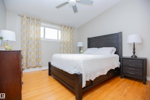 Spacious primary bedroom featuring a dark wood bed frame, wood-finish flooring throughout, and abundant natural light from a transom window - 9107 58 Street Nw, Edmonton, AB - Indoor Photo Showing Bedroom
