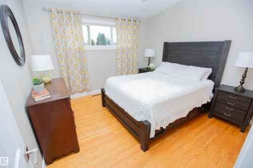 Bright secondary bedroom featuring a wood-finish plank floor, large windows with natural light, and blackout-style curtains in a geometric yellow and cream pattern - 9107 58 Street Nw, Edmonton, AB - Indoor Photo Showing Bedroom