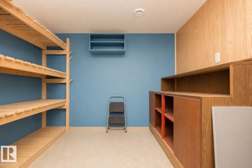 Versatile storage room featuring extensive built-in wooden shelving throughout, warm wood-finish cabinetry with multiple compartments, neutral flooring, and soft recessed ceiling lighting - 9107 58 Street Nw, Edmonton, AB - Indoor