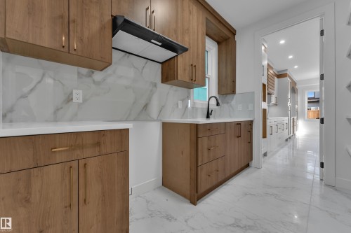 White countertop, wood-finish cabinetry, white marble-patterned backsplash, matte black faucet, and white marble-patterned flooring - 2039 156 Avenue Nw, Edmonton, AB - Indoor Photo Showing Kitchen