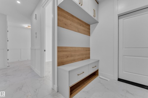 Built-in storage bench with wood-finish backing, upper cabinetry with gold-tone hardware, and white panel doors - 2039 156 Avenue Nw, Edmonton, AB - Indoor Photo Showing Other Room